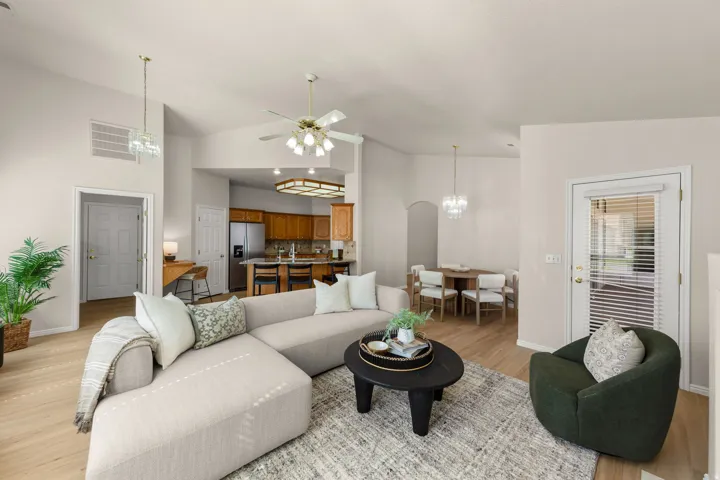 Vaulted ceiling with a ceiling fan, wood-finish flooring, kitchen with wood cabinetry and stainless steel appliances, dining area with chandelier lighting, and a glass-paneled door