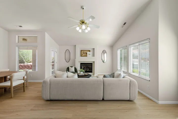 Vaulted ceiling with an attached ceiling fan, recessed fireplace with a mantel, wood-finish flooring, and multiple windows
