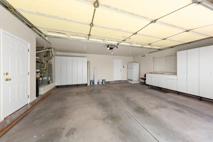 2-CAR - Spacious garage featuring a concrete floor, built-in white cabinetry, a built-in workbench area, a window with blinds, and white interior doors