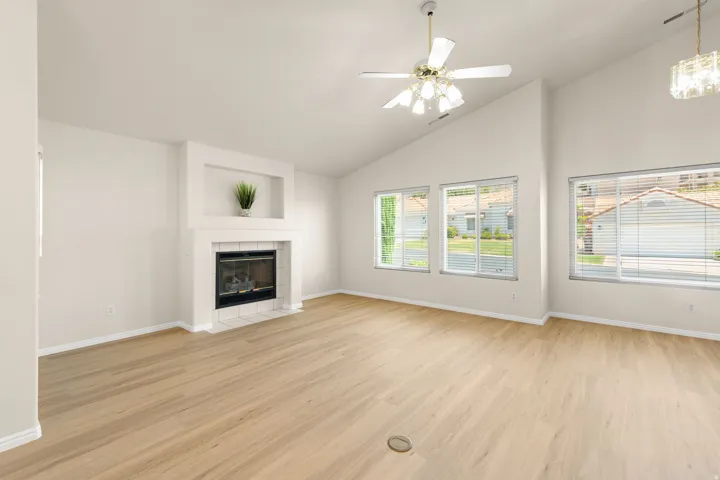Spacious living area featuring a fireplace with built-in shelving, wood-finish flooring, vaulted ceilings, and multiple windows with blinds