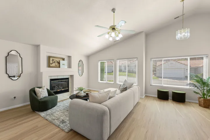 Vaulted ceiling with a ceiling fan, fireplace with a tile surround, built-in recessed shelf, wood-finish flooring, and multiple windows