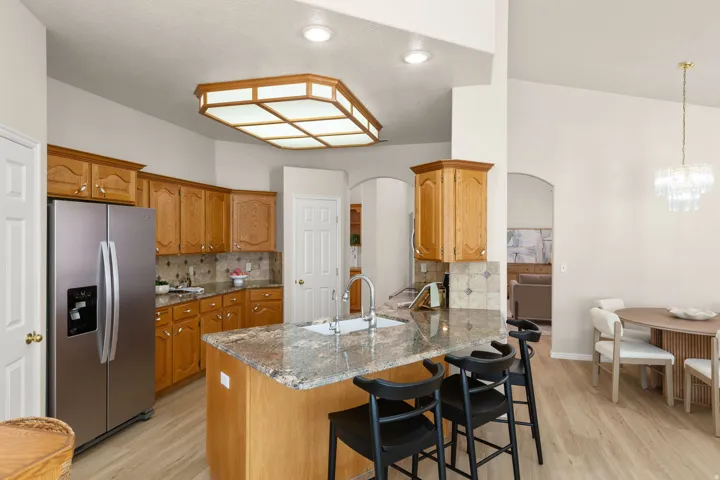 Kitchen featuring wood cabinetry, stainless steel refrigerator, stone countertops, and a central island with a sink