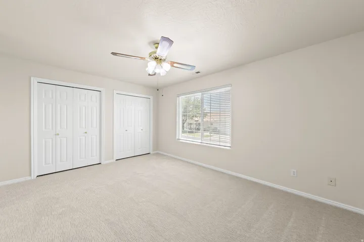 GUEST BEDROOM 1 - Carpeted room featuring a ceiling fan, two sets of bi-fold closet doors, a window with horizontal blinds, and neutral wall paint