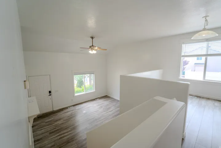 Vaulted ceiling with a ceiling fan, wood-finish flooring, white walls, and a large window with blinds