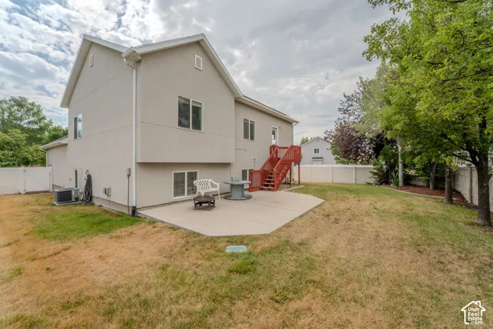 Expansive backyard featuring a concrete patio, red-stained wooden deck and stairs, and a white privacy fence