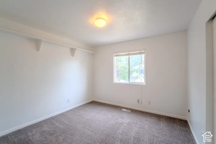 Neutral-toned room featuring a single window with blinds, overhead lighting, carpet flooring, and white baseboards