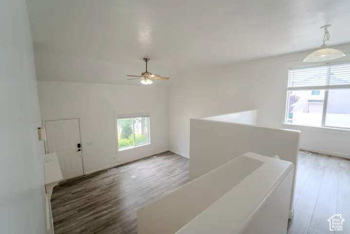 Vaulted ceiling with a ceiling fan, wood-finish flooring, white walls, and a large window with blinds