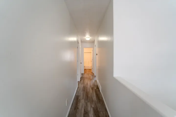 Hallway featuring wood-finish flooring, white painted walls, and overhead lighting