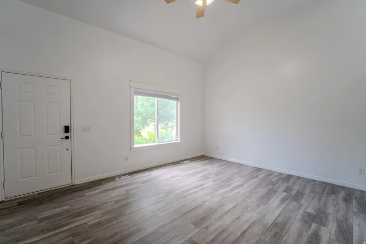 Spacious room featuring vaulted ceilings, a contemporary ceiling fan, and wood-finish flooring