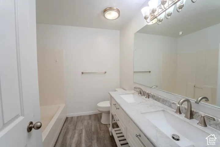 Bathroom featuring a dual vanity with a stone countertop, brushed nickel fixtures, a wide mirror, wood-finish flooring, and a tub-shower combination with subway tile surround