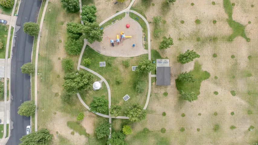 Neighborhood park featuring a playground area with soft ground cover, paved walking paths, a gazebo, and a shaded structure