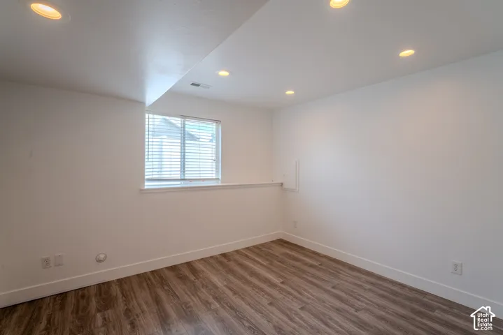 Spacious room featuring neutral wall tones, recessed lighting, wood-finish flooring, a window with horizontal blinds, and white baseboards