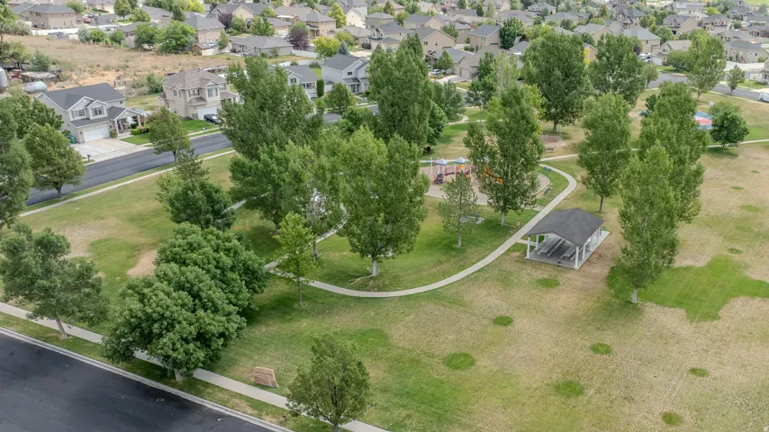 Expansive green space featuring a paved walking path, mature trees, and a covered picnic structure
