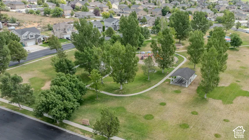 Expansive green space featuring a paved walking path, mature trees, and a covered picnic structure