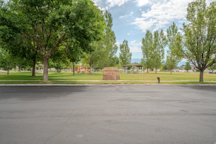 Expansive community park featuring a stone monument with "PRIVATE PARK" inscription, mature trees, a covered pavilion, and a playground structure
