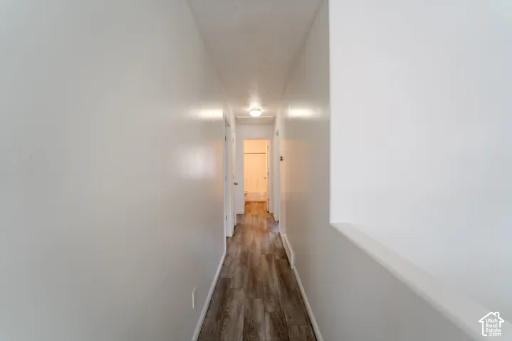 Hallway featuring wood-finish flooring, white painted walls, and overhead lighting