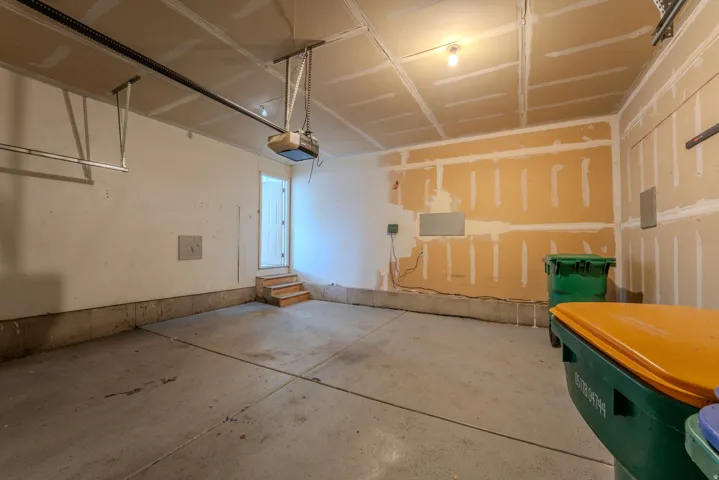 Concrete floor garage featuring an automatic garage door opener, a side entry door with wooden steps, and overhead lighting