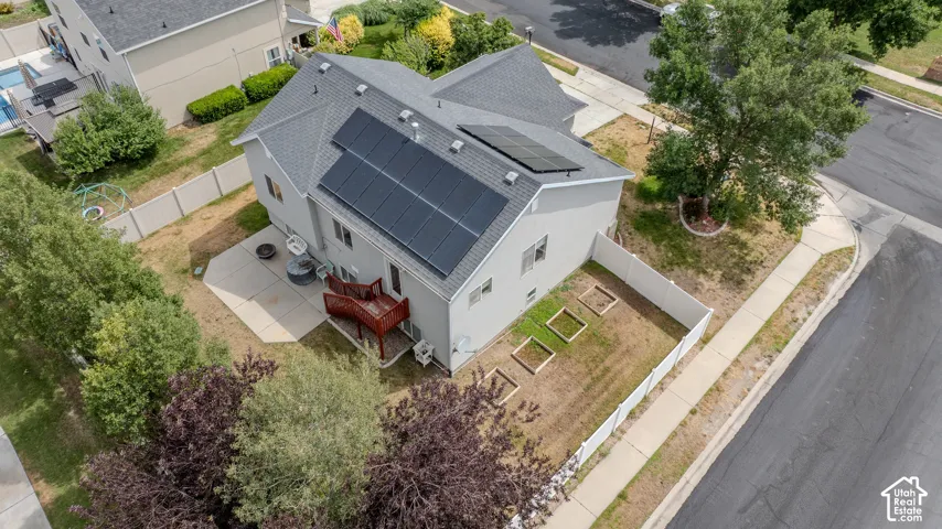 Rear exterior featuring a large array of rooftop solar panels, a concrete patio, a wood deck with stairs, and raised garden beds