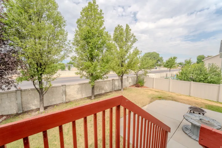 Private backyard featuring a concrete patio, red wood-finish railings, mature trees, and a block retaining wall