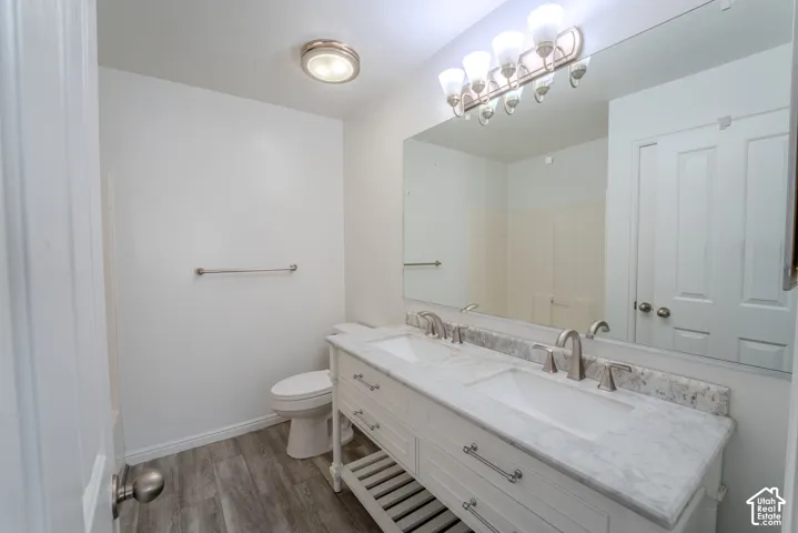 Bathroom featuring a dual vanity with a marble-finish countertop, brushed nickel fixtures, wood-finish flooring, a contemporary light fixture, and a large wall-mounted mirror