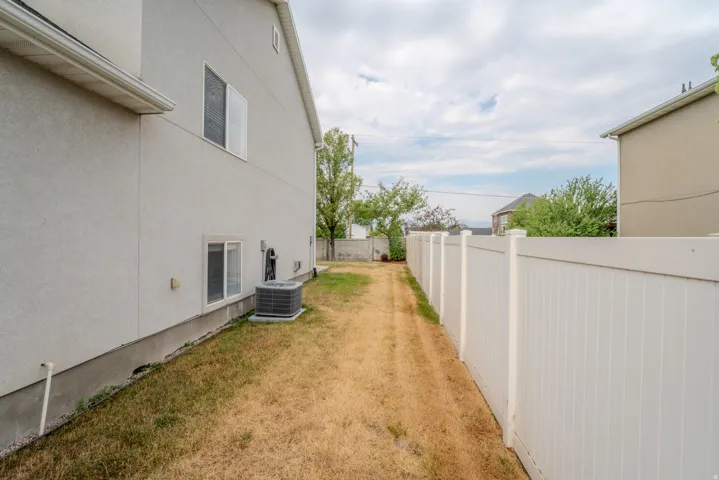 Side yard featuring a stucco exterior, multiple windows, an air conditioning unit, and a white privacy fence