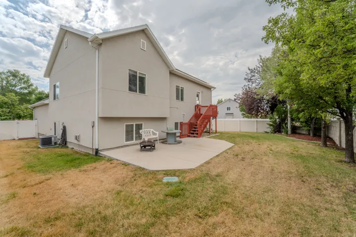Expansive backyard featuring a concrete patio, red-stained wooden deck and stairs, and a white privacy fence
