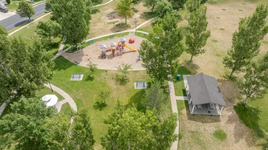 Expansive green space featuring a playground with multiple slides and climbing structures, a covered pavilion with picnic tables, and paved walking paths