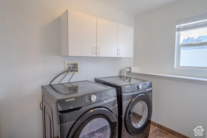 Laundry area featuring white cabinetry, a window with natural light, a utility hookup, and a tiled floor