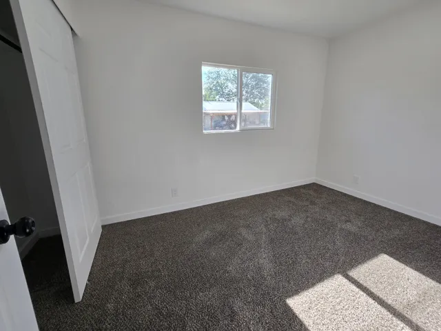 Bright room featuring light-colored walls, a double-hung window, white trim, and dark textured carpeting