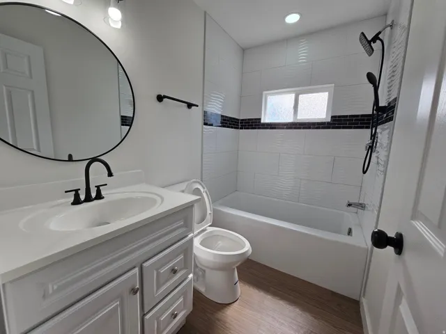 Bathroom featuring a white vanity with integrated sink, black hardware, a round mirror, and wood-finish flooring