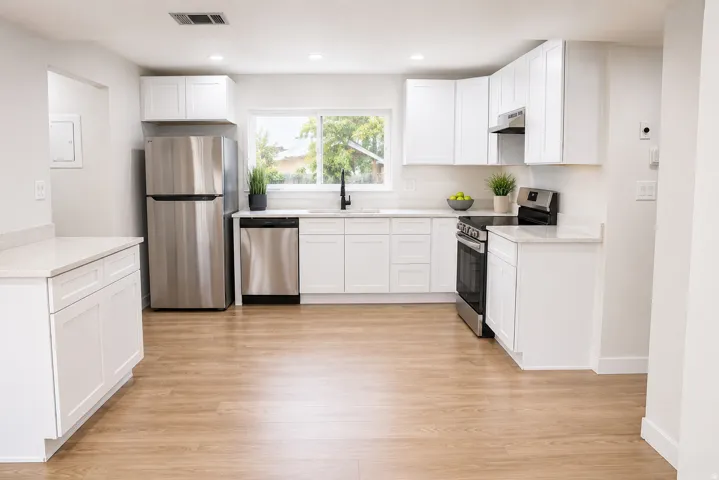 Bright kitchen featuring white shaker cabinetry, light countertops, wood-finish flooring, and stainless steel appliances including a refrigerator, dishwasher, and range with hood