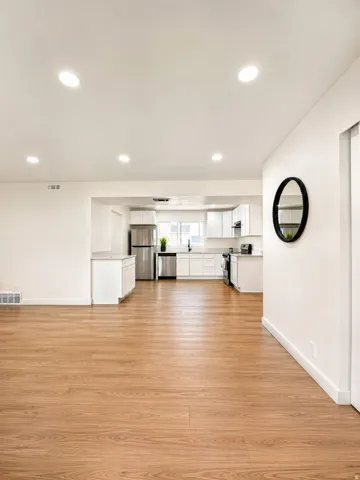Open-concept living space featuring wood-finish flooring, recessed lighting, a modern kitchen with white cabinetry, and stainless steel appliances