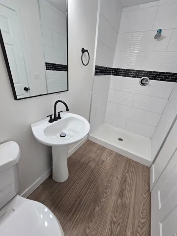 Pedestal sink with matte black hardware, framed mirror, and wood-finish flooring