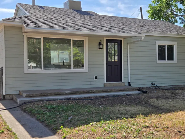 Exterior showcasing light green horizontal siding, a dark paneled front door with glass inserts, white window trim, and a shingled roof