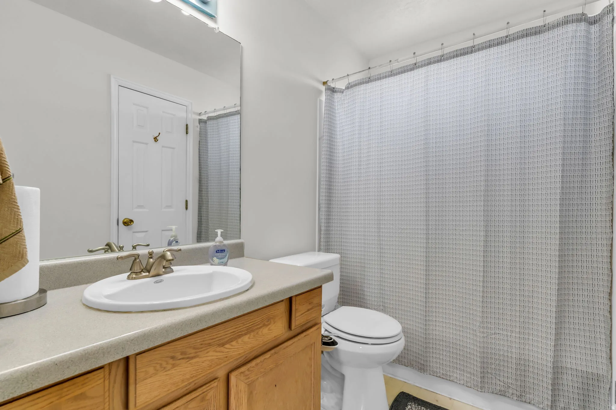 Bathroom featuring a wood-finish vanity with a light-toned countertop, an oval undermount sink, and a mirrored wall