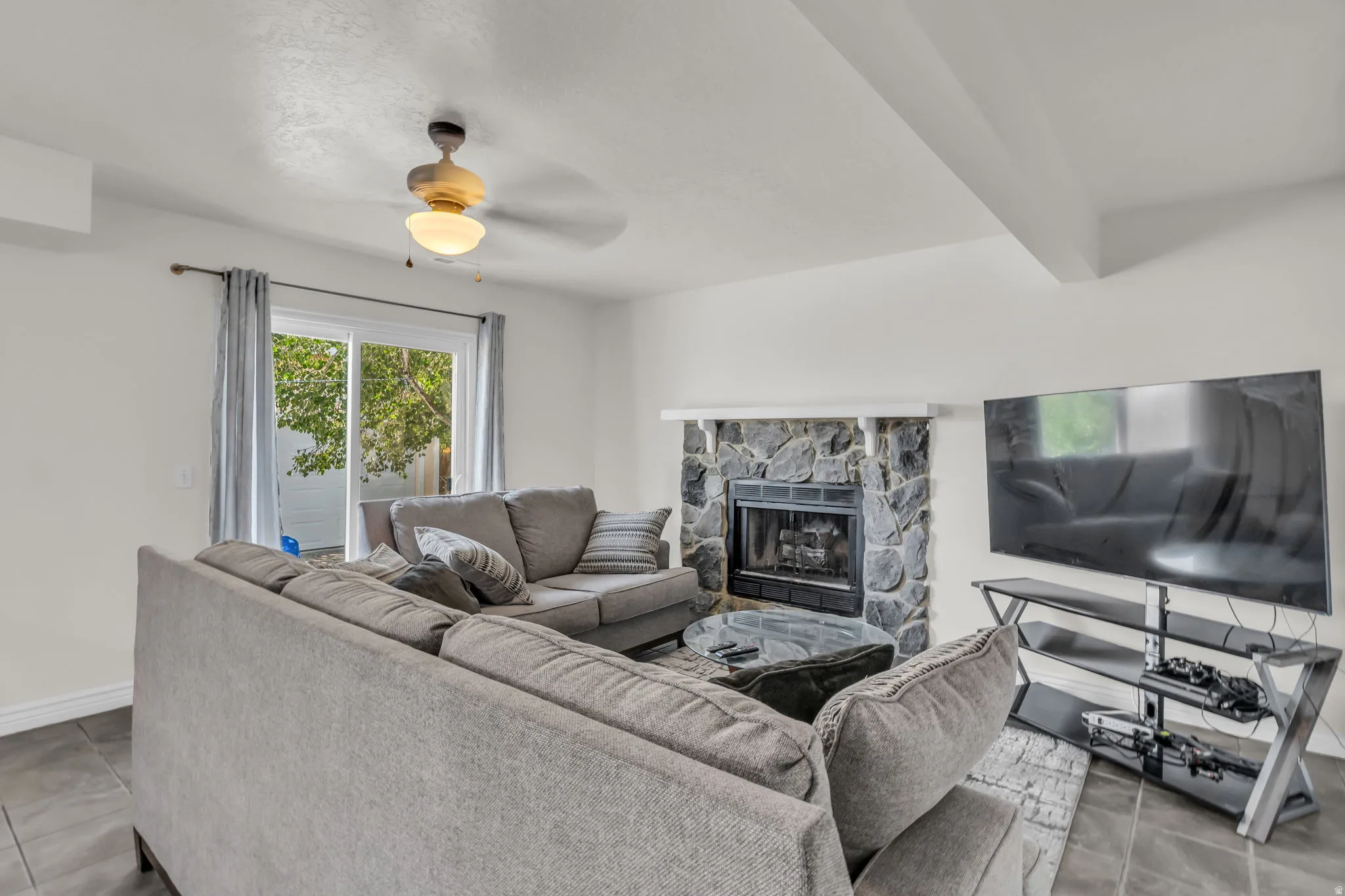 Living area featuring a stone fireplace, dark tile flooring, and a ceiling fan with integrated lighting