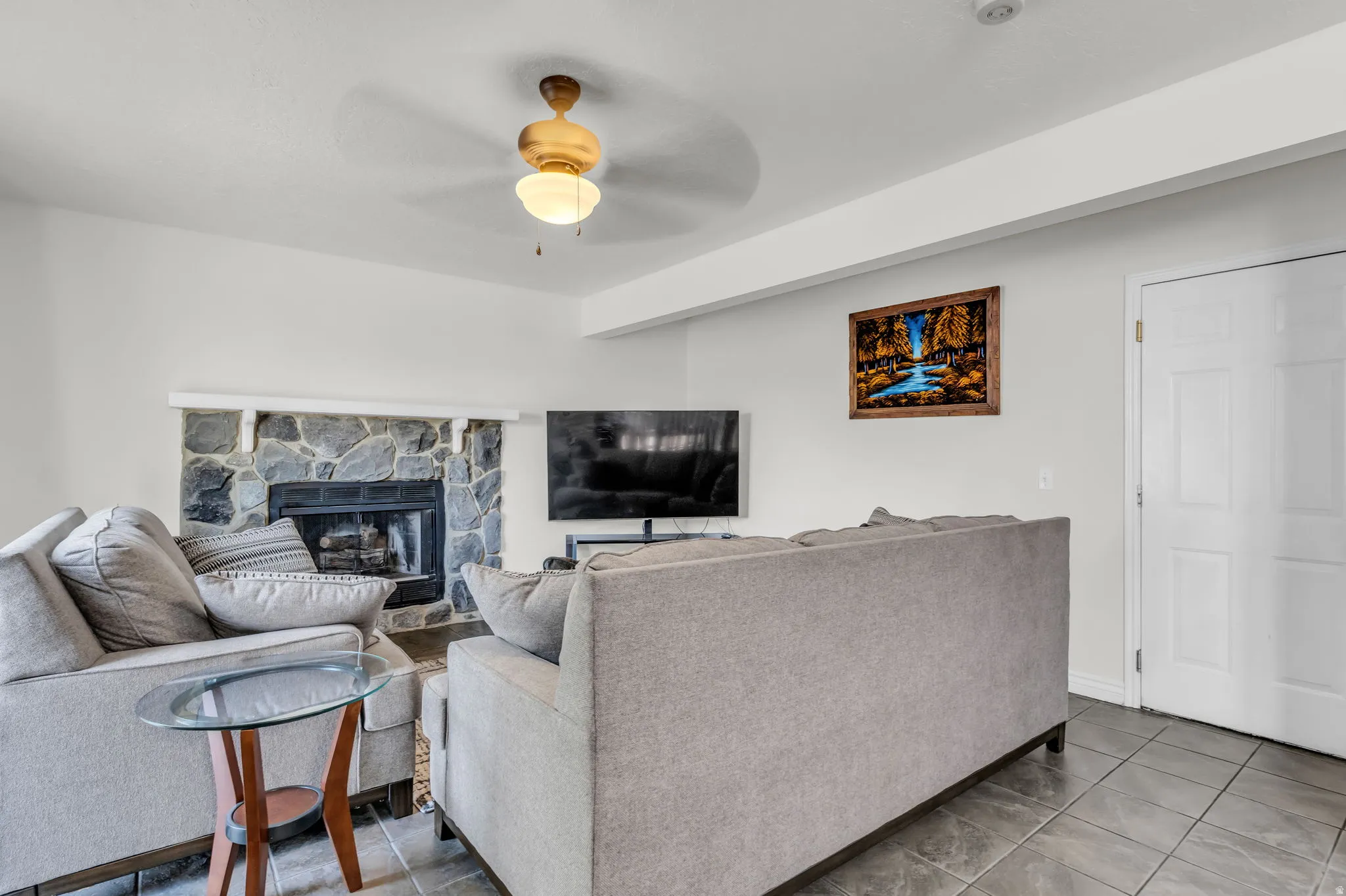 Living area featuring a stone-clad fireplace with a dark hearth, ceiling fan with integrated lighting, and durable tile flooring