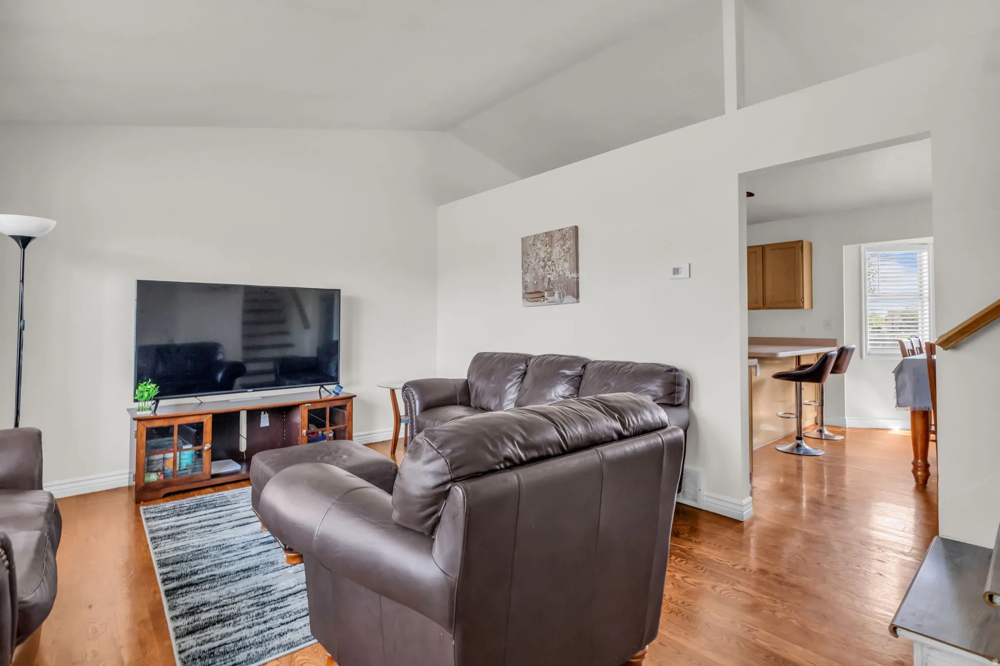Living area featuring vaulted ceilings, light-toned walls, and wood-finish flooring