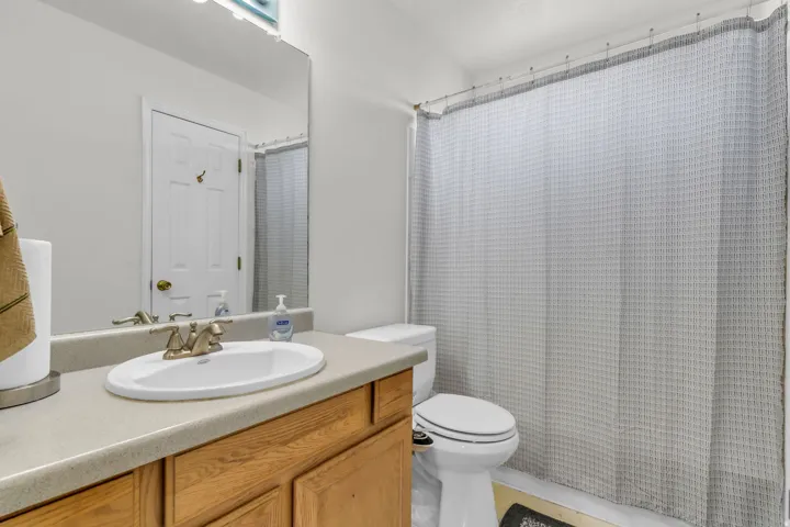 Bathroom featuring a wood-finish vanity with a light-toned countertop, an oval undermount sink, and a mirrored wall