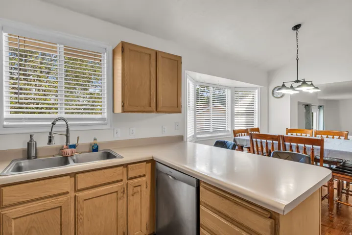 Kitchen featuring a double stainless steel sink with a high-arc faucet, wood-finish cabinetry, light-toned countertops, and a built-in dishwasher