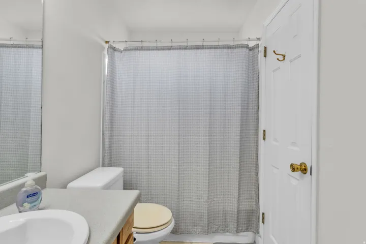 Bathroom featuring a shower with a gray patterned curtain, white panel door with brass hardware, vanity with a light-colored countertop, and an integrated white sink