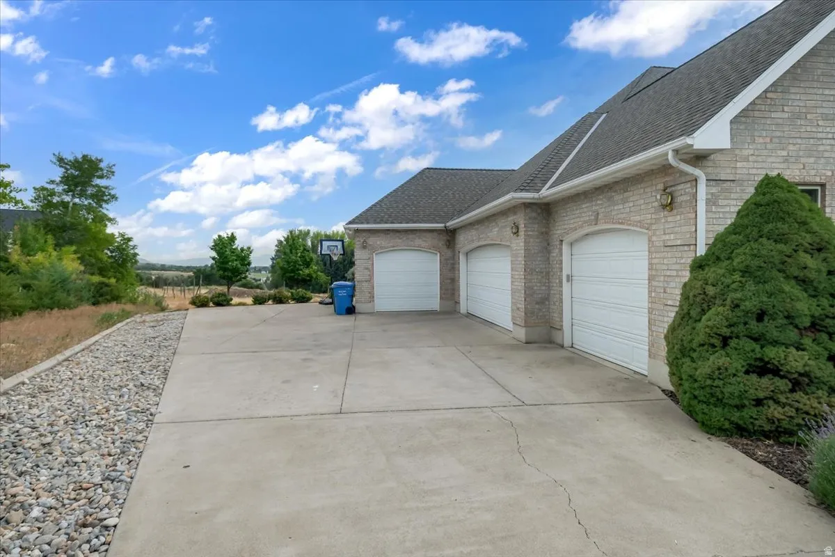 Spacious concrete driveway featuring a three-car garage with arched entryways and a brick exterior