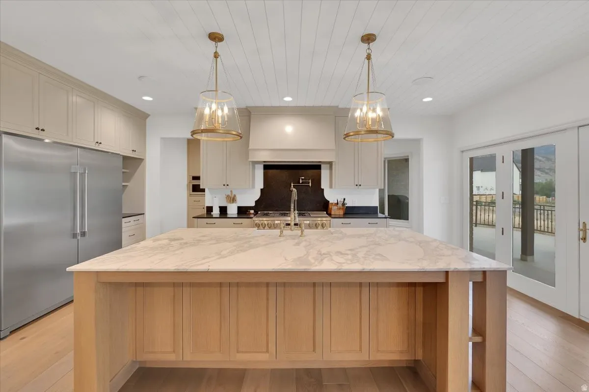 Gourmet kitchen featuring a substantial wood island with a substantial stone countertop, stainless steel refrigerator, white cabinetry, brass pendant lighting, and light wood-finish flooring
