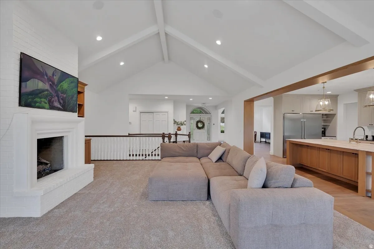 Vaulted ceilings with exposed beams, white brick fireplace with a mantle, recessed lighting, wood-finish flooring, and a kitchen island with pendant lighting