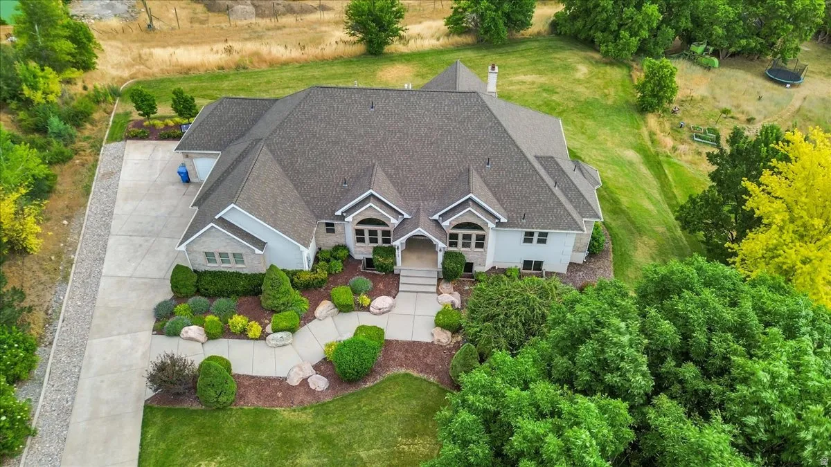 Expansive property featuring a multi-gabled roofline, stone and siding exterior, a concrete driveway, established landscaping with mature trees, and a manicured lawn