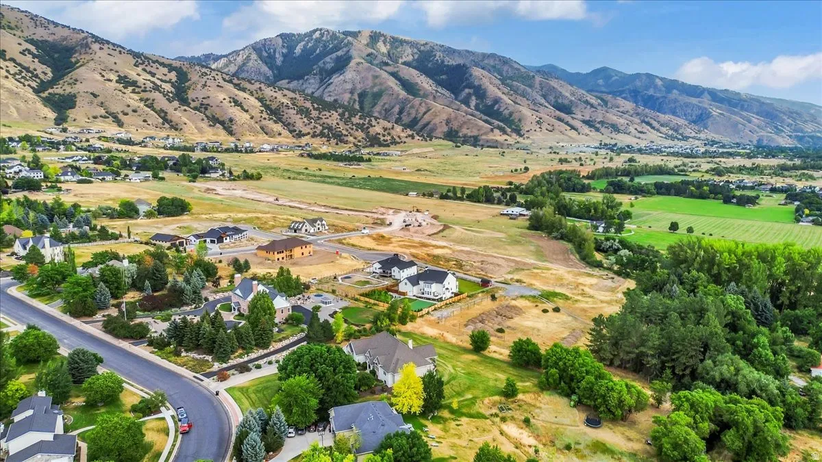 Expansive valley setting with mountainous backdrop, featuring a residential neighborhood, green fields, and scattered trees