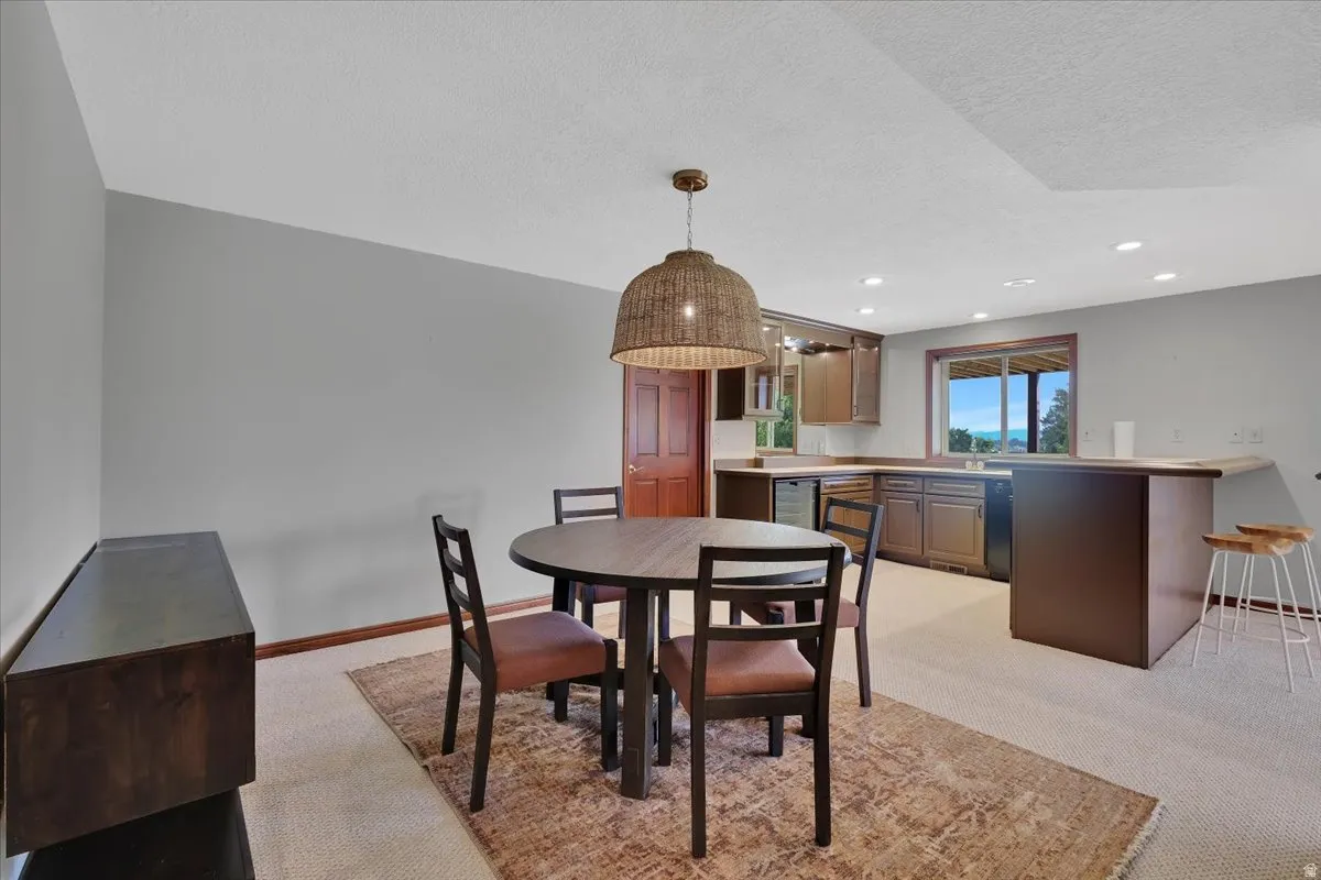 Lower-level entertainment space featuring a built-in wet bar with wood cabinetry, a window with a distant natural landscape, recessed ceiling lighting, and light-toned carpet flooring