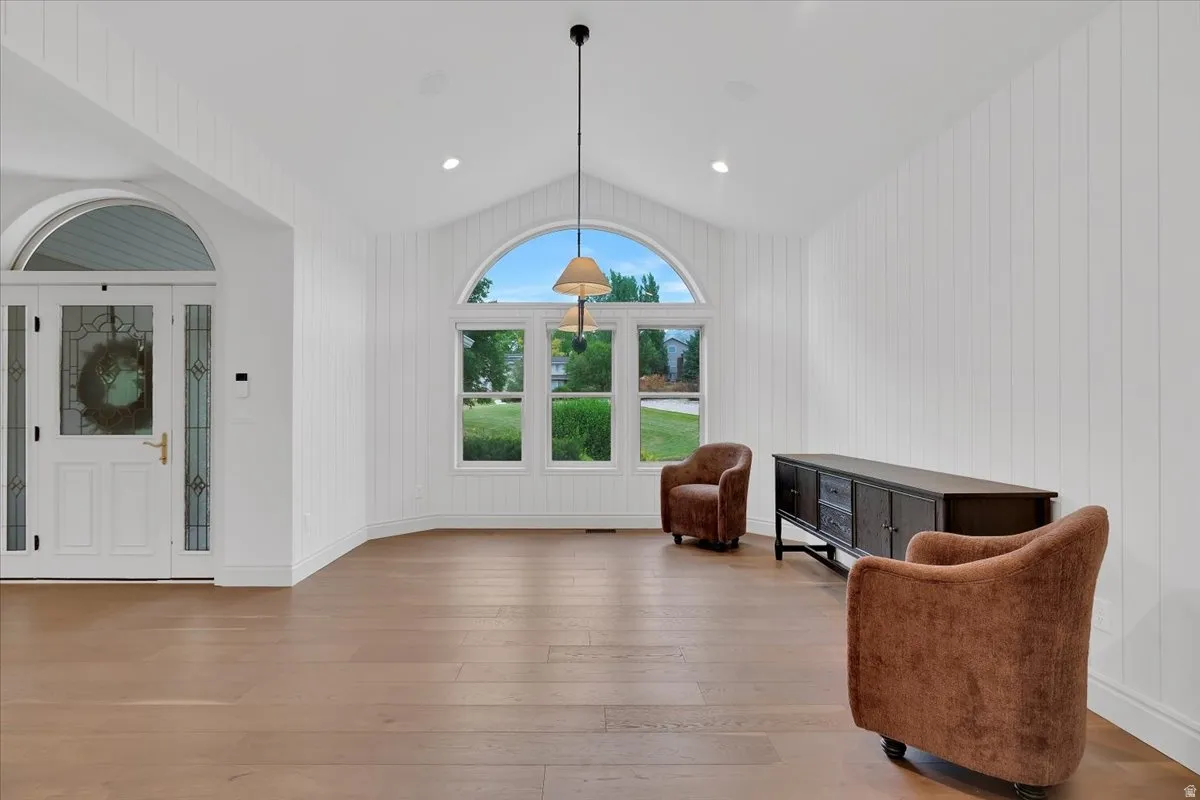 Expansive room featuring vaulted ceilings, a prominent arched window, and wood-finish flooring