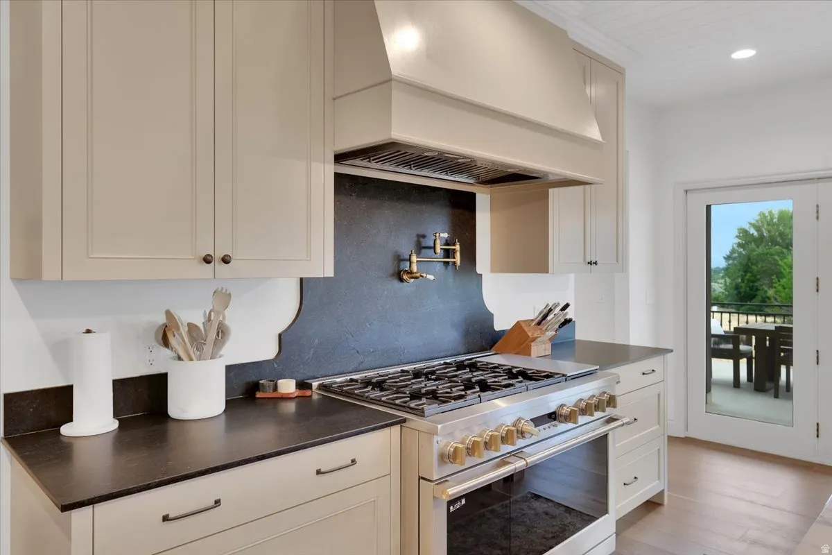 Gourmet kitchen featuring a professional-grade stainless steel range with gold-tone hardware, dark countertop surfaces, a pot filler, custom cabinetry, and wood-finish flooring