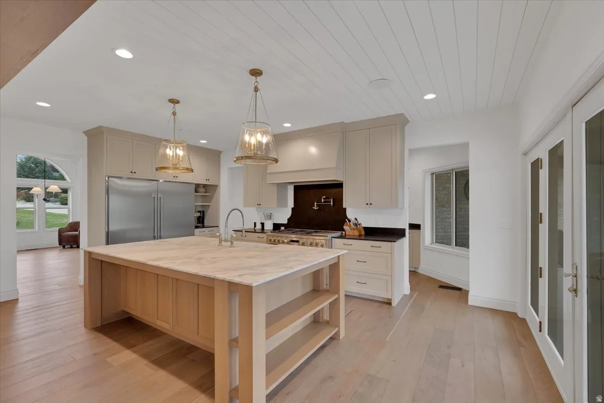 Gourmet kitchen featuring a large central island with a light-toned countertop, stainless steel refrigerator and range, shaker-style cabinetry, and wood-finish flooring